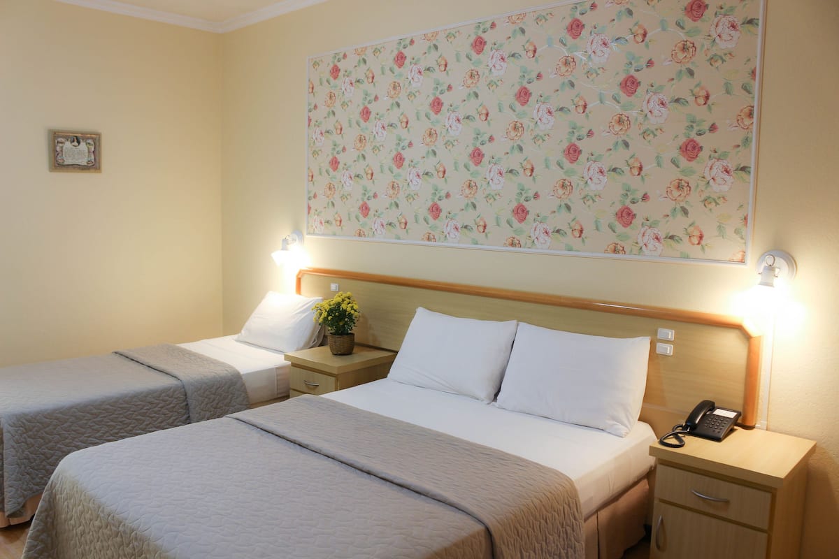 A hotel room with two beds, a floral wallpaper, bedside lamps, a nightstand with a phone, and a small plant.