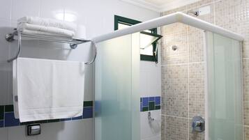 Casa de banho com cabine de chuveiro em vidro, um porta-toalhas com toalhas dobradas e parede revestida com detalhes em verde.