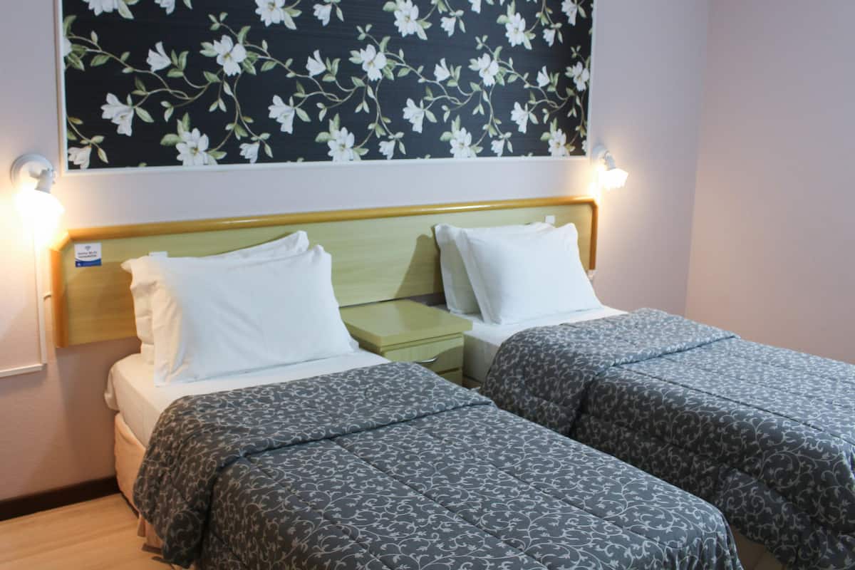 A double bed with a wooden headboard, two bedside tables, and a floral-patterned wall above.