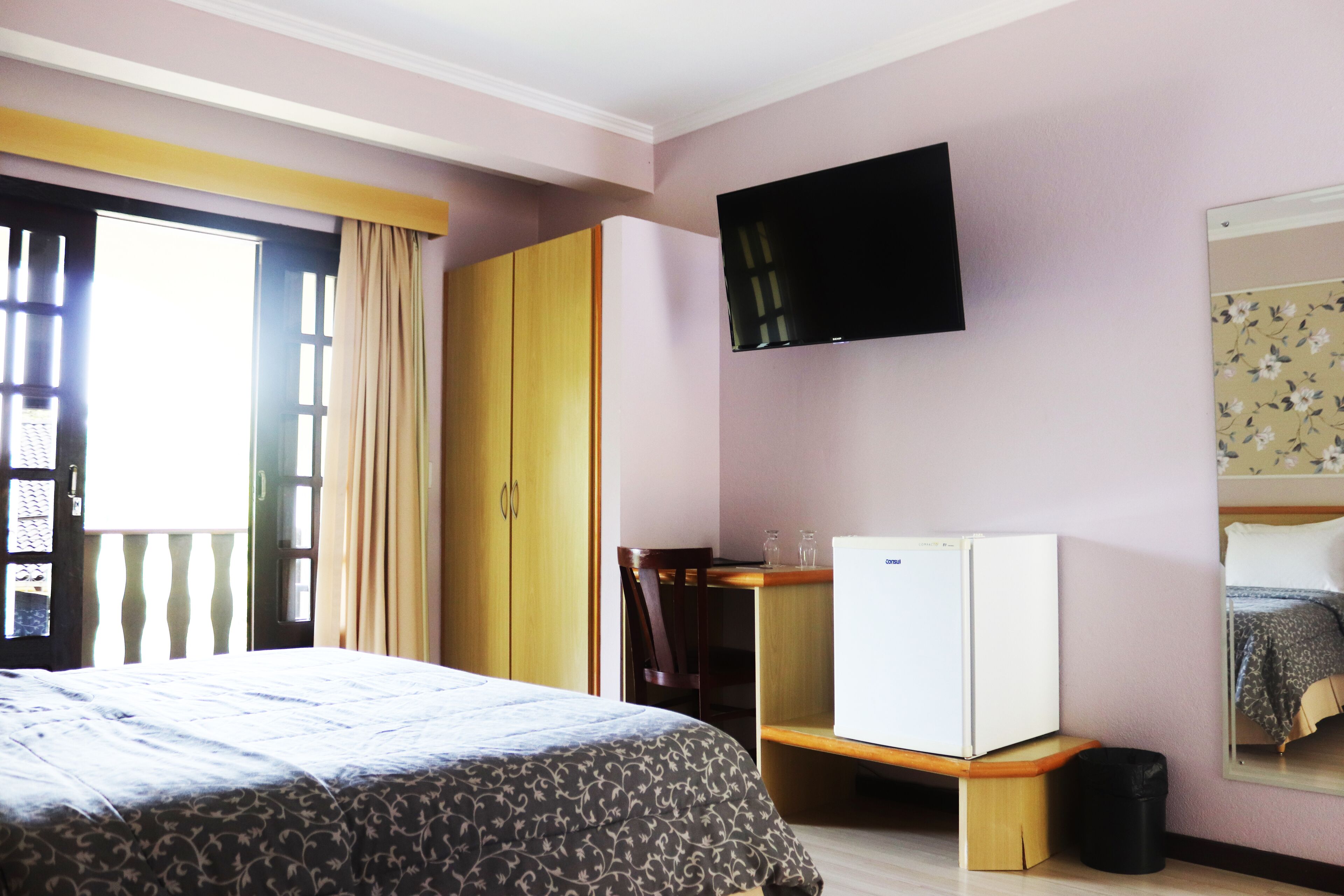 A bedroom with a bed, wardrobe, desk, and a television.