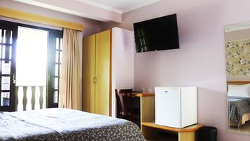 A bedroom with a bed, wardrobe, desk, and a television.