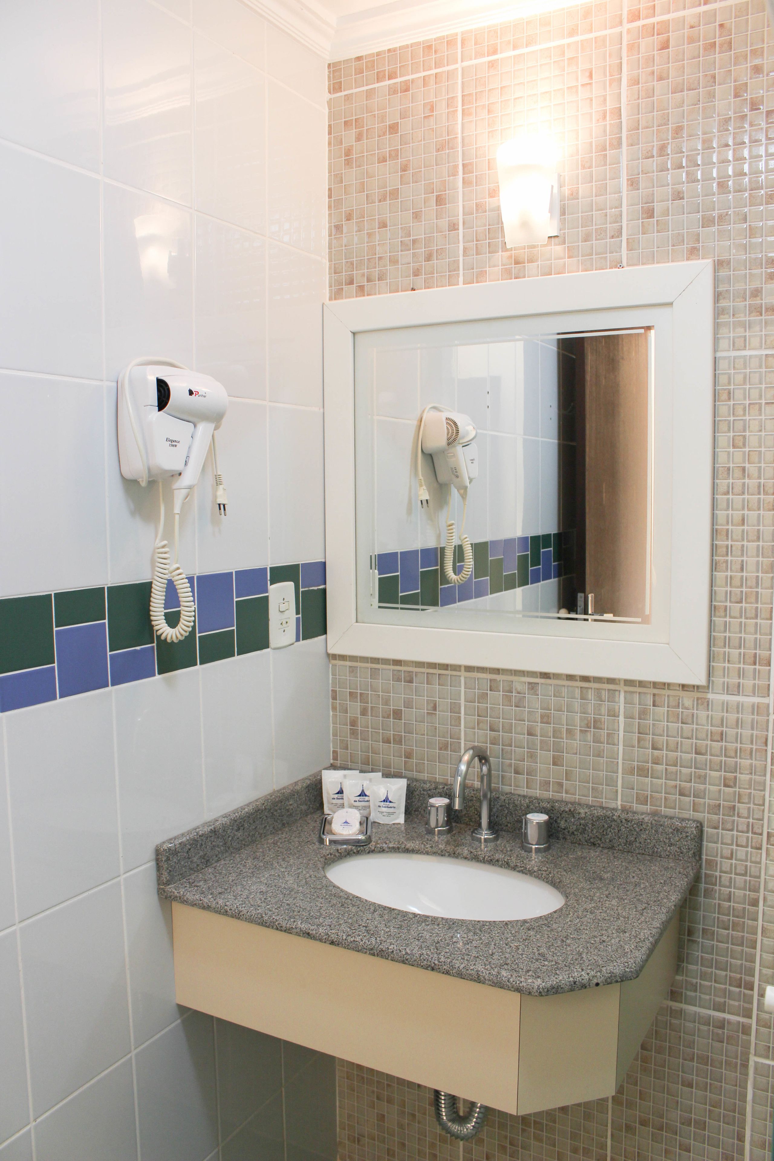 Un baño con lavamanos, espejo y secador de pelo fijado en la pared.