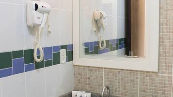 Un baño con lavamanos, espejo y secador de pelo fijado en la pared.
