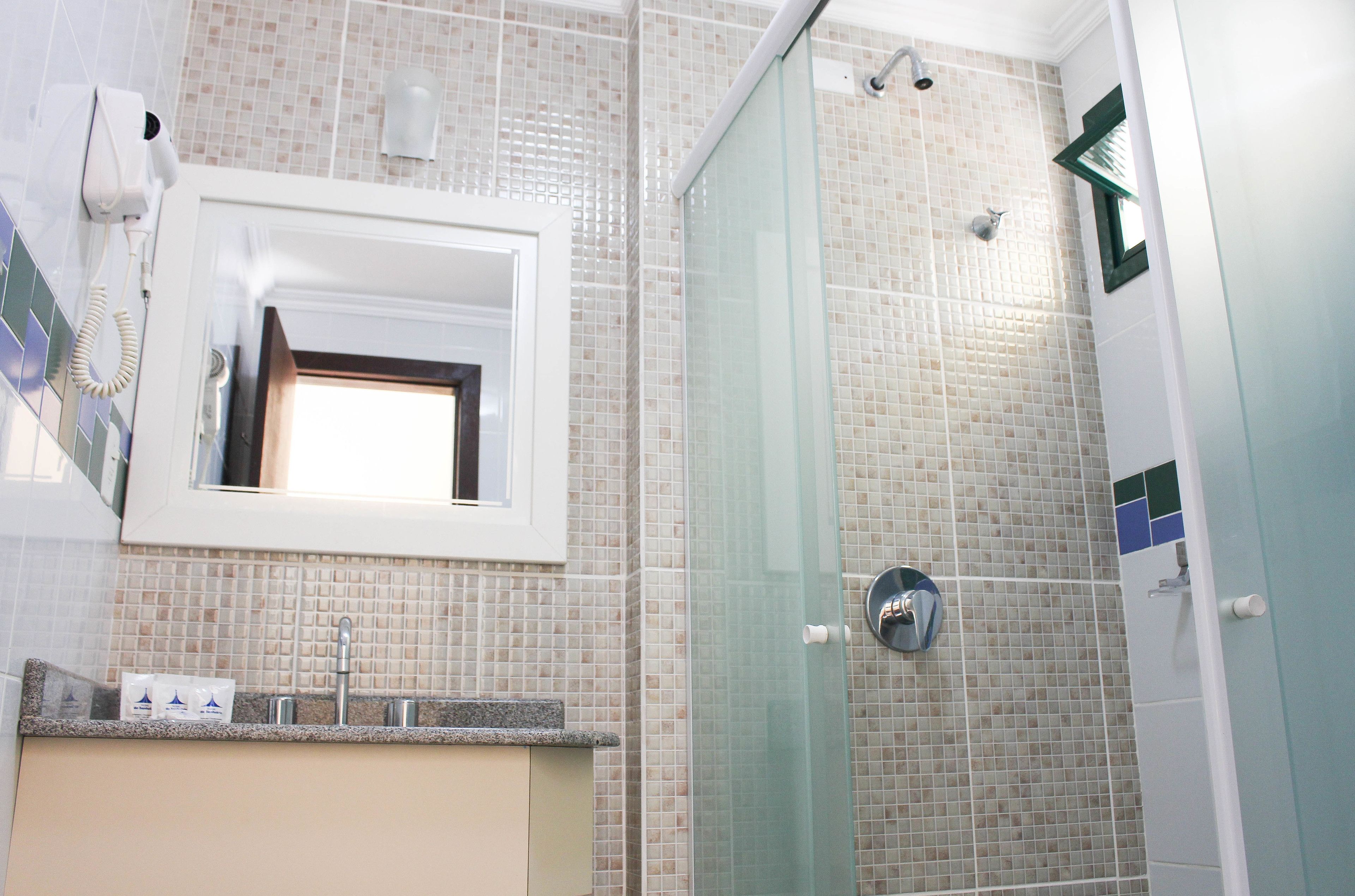 Un baño con cabina de ducha de vidrio, un lavamanos con espejo y un secador de pelo montado en la pared.