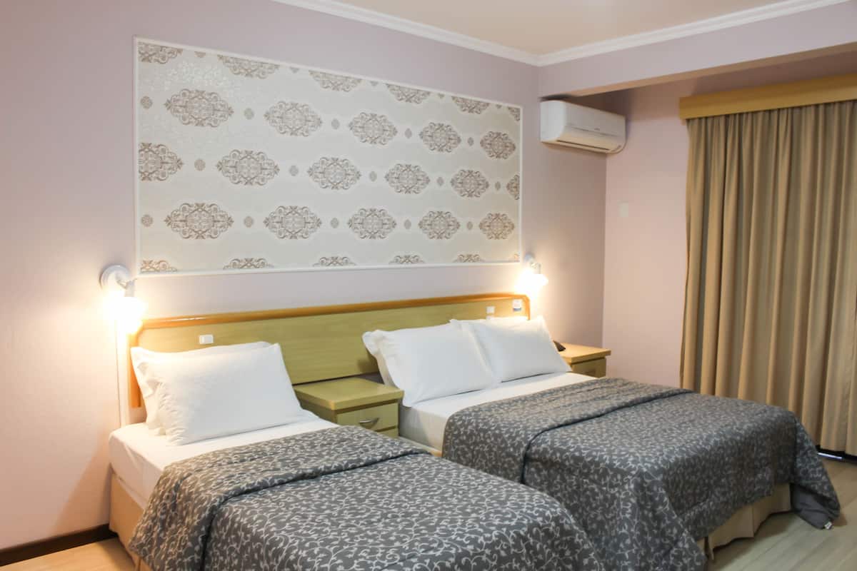A hotel room with two beds, a patterned headboard, a nightstand, and a window with curtains.