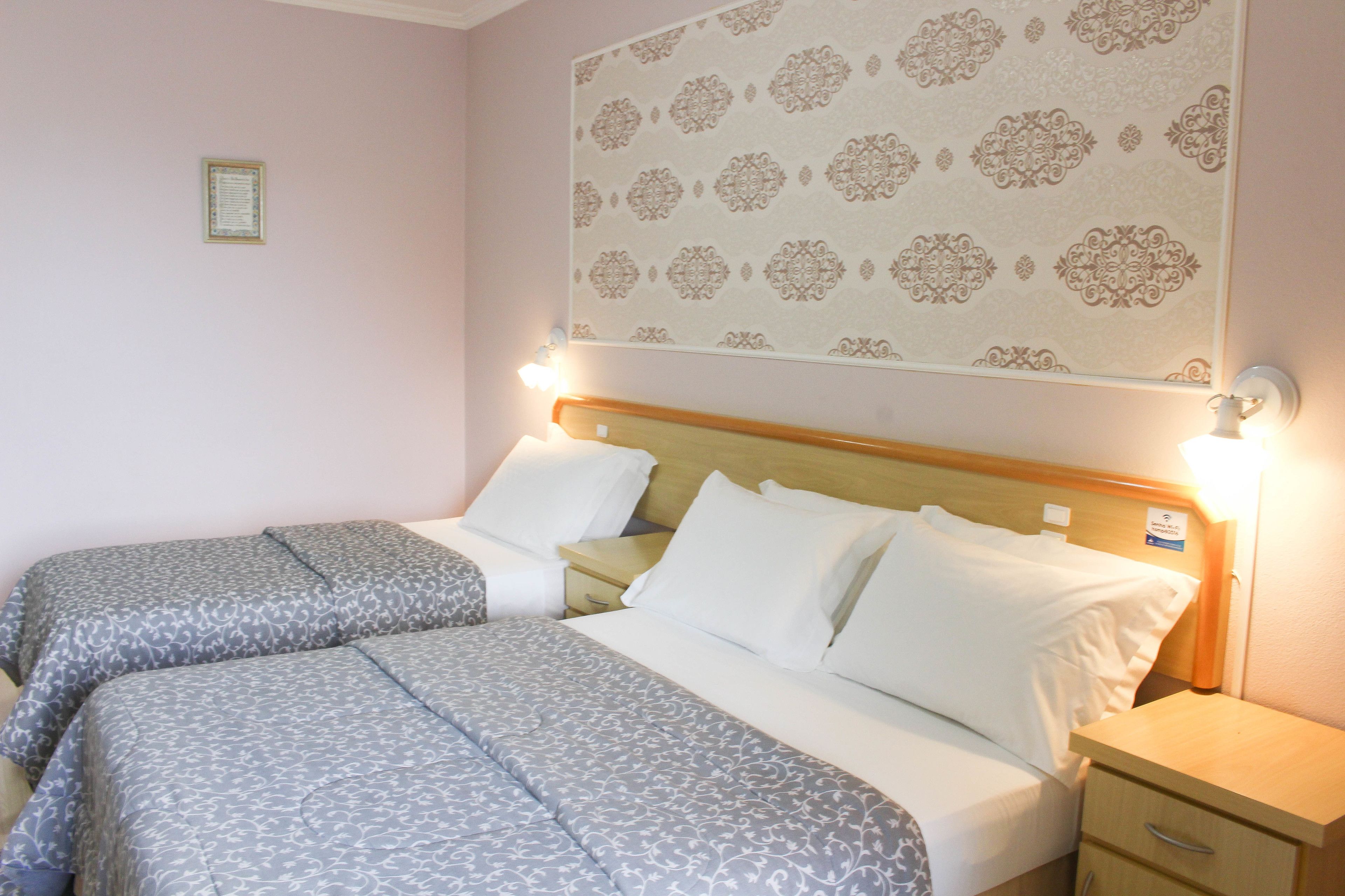 Habitación de hotel con dos camas, cabeceros de madera, mesitas de noche y un tapiz decorativo en la pared.