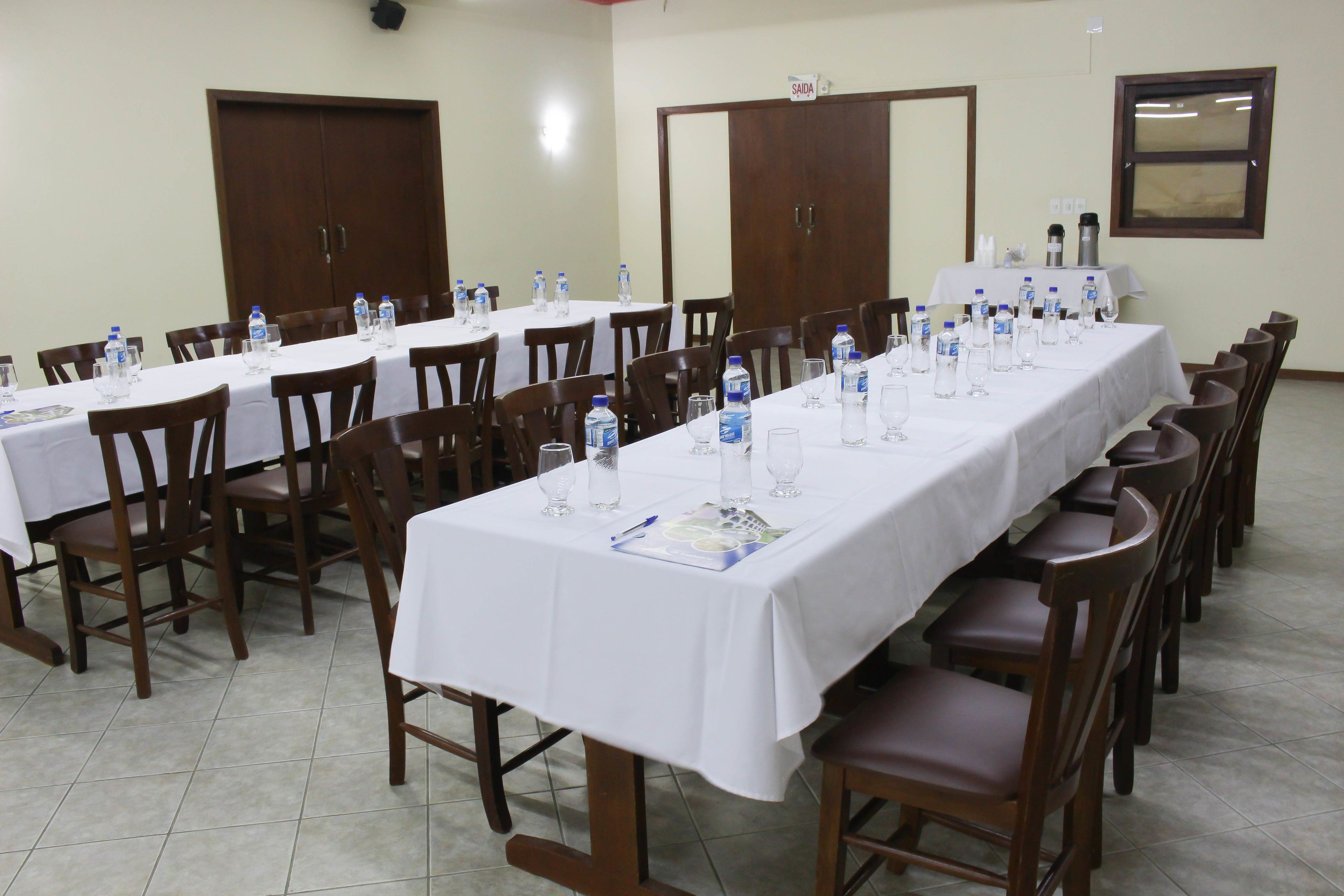 Un salón de conferencias con varias mesas, cada una con botellas de agua, vasos y una placa de identificación.