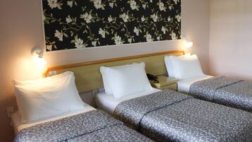 Una habitación de hotel con dos camas, cada una con almohadas blancas y un edredón estampado. El papel tapiz de flores adorna la pared detrás de las camas.