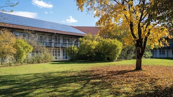 Um edifício com telhado solar, rodeado por um espaço gramado com árvores e arbustos.