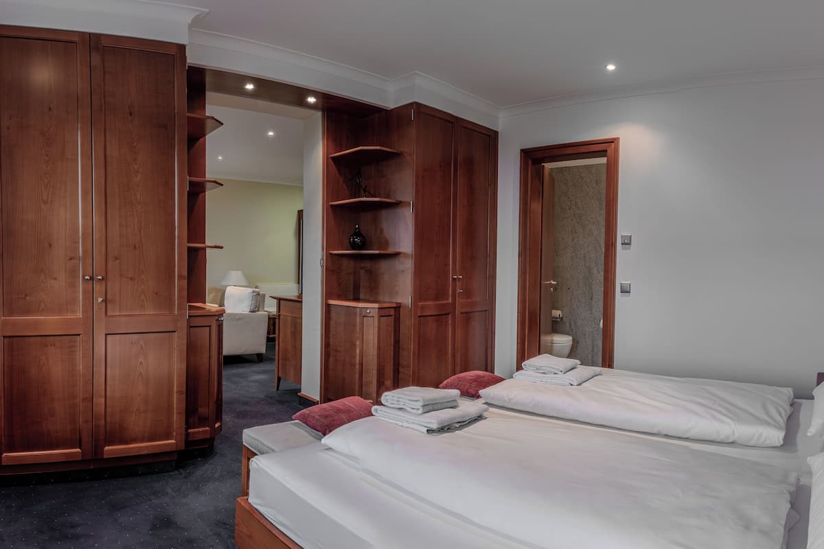 A hotel room with two beds, wooden wardrobes, a bathroom, and a hallway leading to another room.