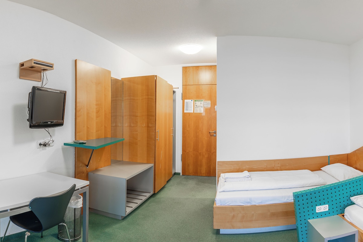 Een hotelkamer met een bed, een bureau, een televisie en een douche.