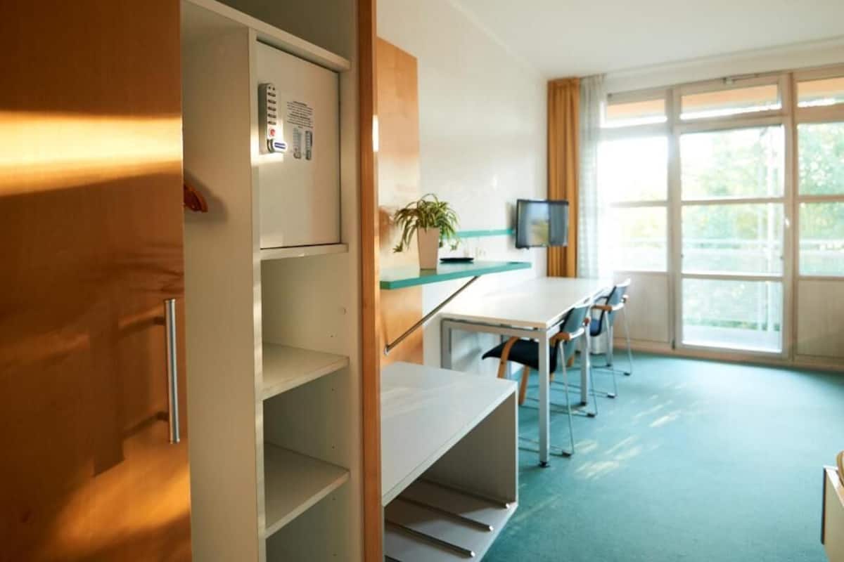 A modern room with a desk, chairs, a television, and a window with curtains.