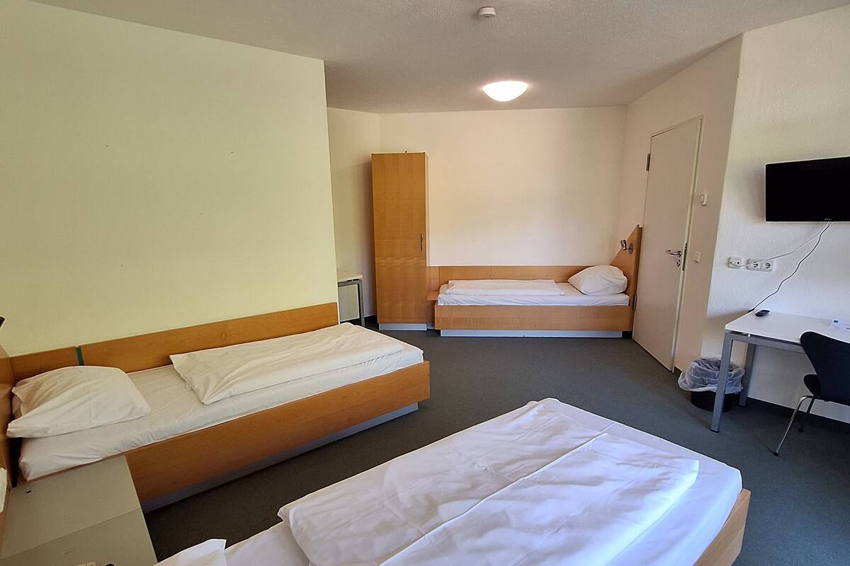 A hotel room with two single beds, a desk, a chair, a TV mounted on the wall, and a wardrobe.