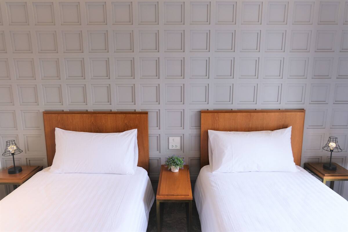 Une chambre d’hôtel avec deux lits, une petite table avec une lampe et un mur orné d’un motif géométrique.