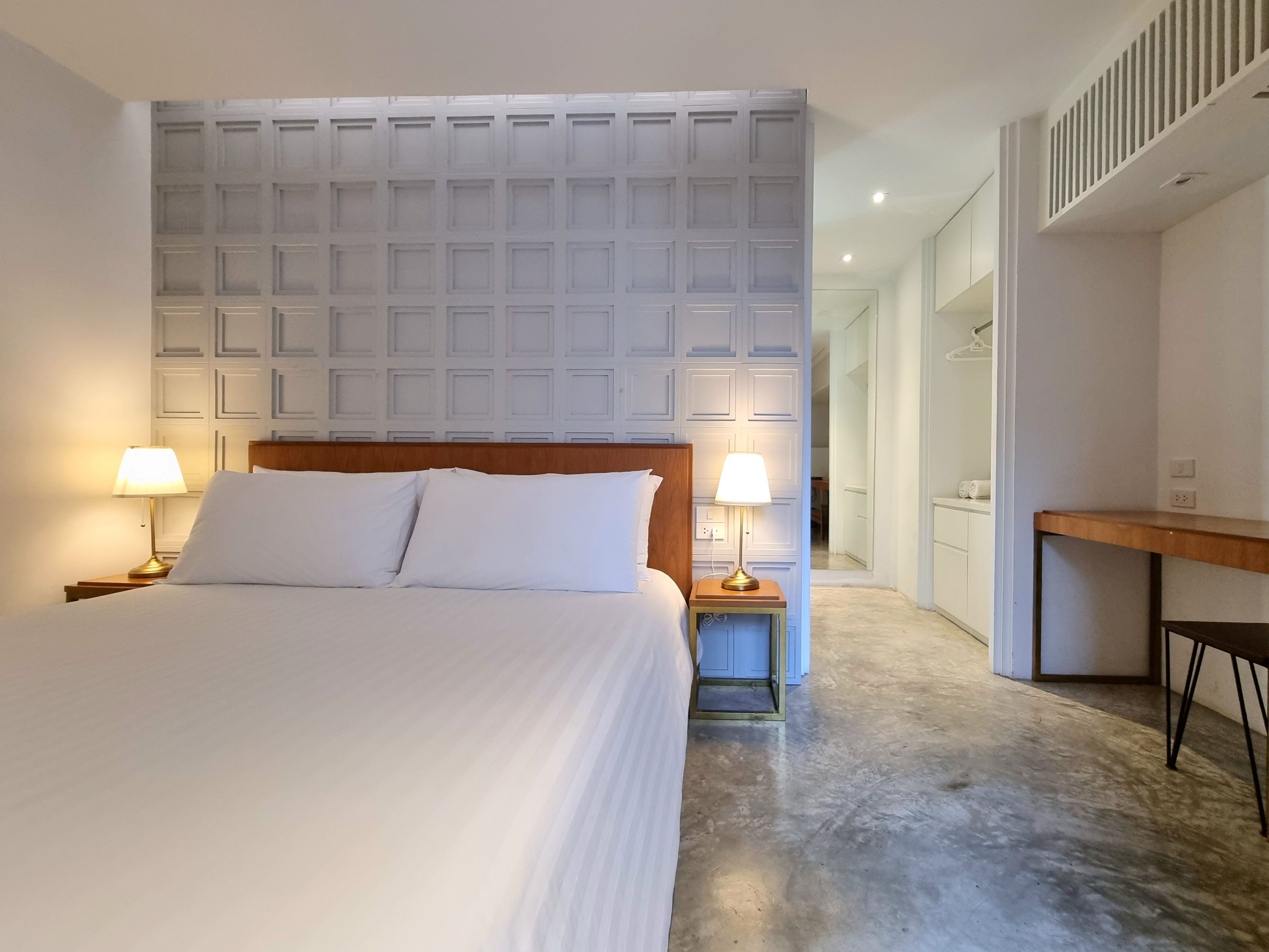 Habitación de hotel con una cama grande, dos lámparas de noche, cabecera de madera y un pequeño escritorio con silla.