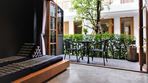 Um quarto moderno com uma cama grande, vista para um pátio com uma árvore e cadeiras, e uma porta de vidro deslizante que dá para uma área externa.
