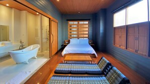 Quarto moderno com uma cama grande, um banco de madeira, uma banheira e um guarda-roupa com portas deslizantes.