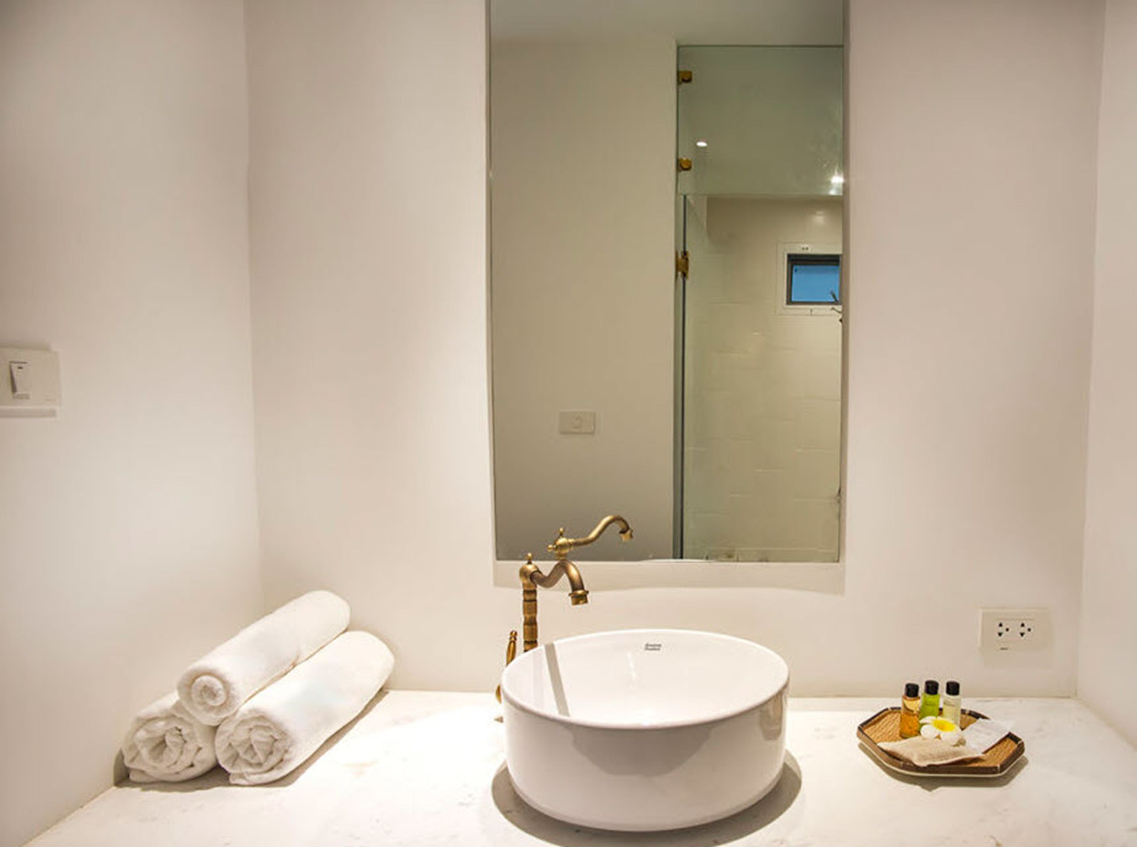 A bathroom with a round white sink, a mirror, and a towel rack with rolled towels.