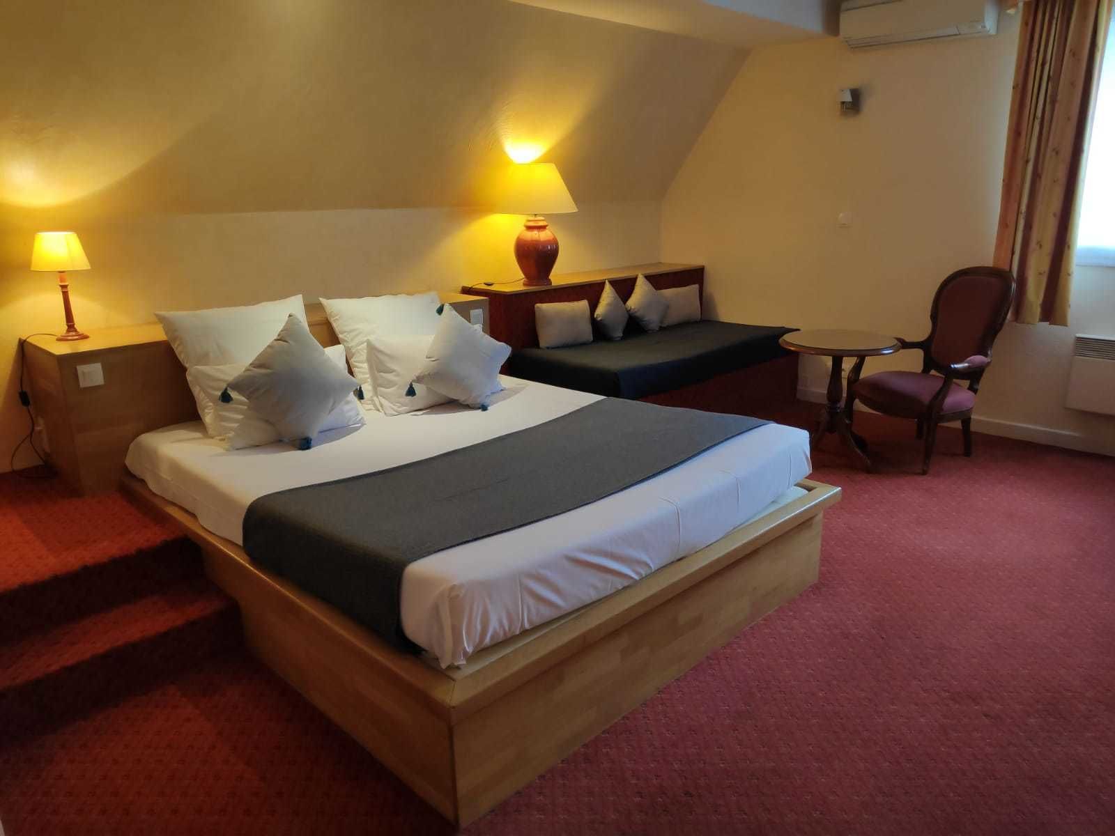 Een hotelkamer met een groot bed, een kleiner bed, een bureau, een stoel en een lamp.