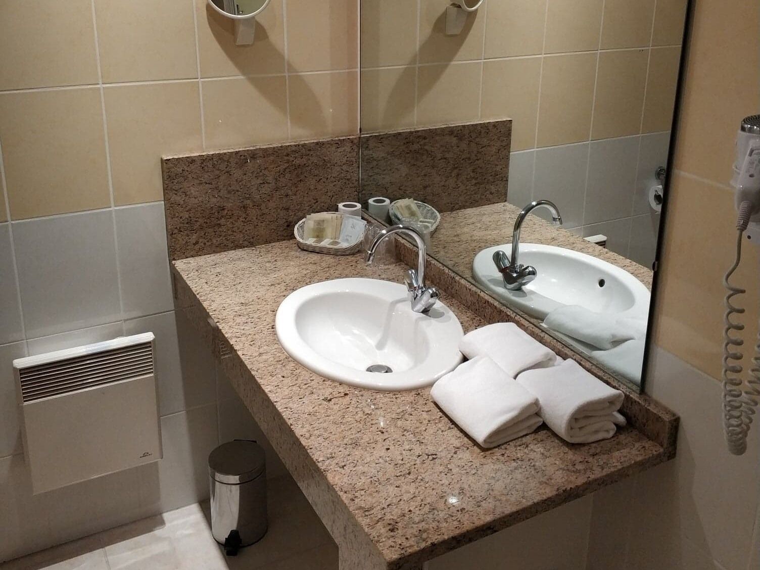Un baño con encimera de granito, dos lavamanos, un espejo y un perchero para toallas.