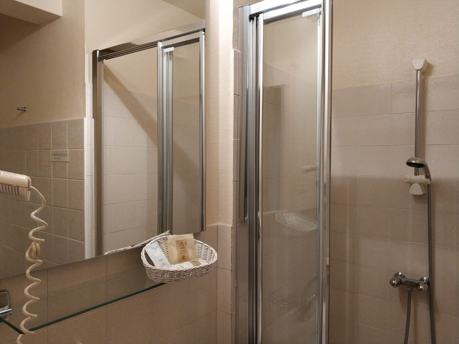 A bathroom with a glass shower enclosure, a towel rack, and a basket on the wall.
