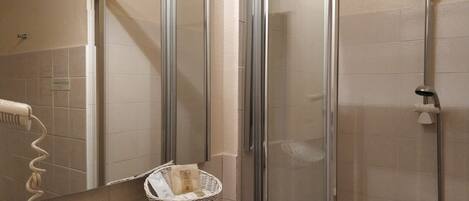 Un baño con cabina de ducha de vidrio, un perchero y una cesta en la pared.