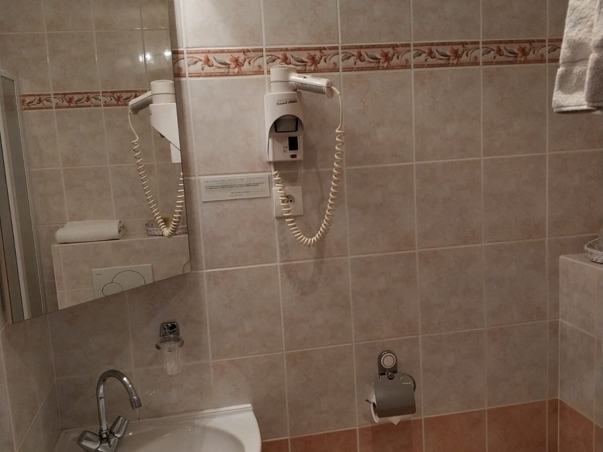 Een badkamer met een wastafel, spiegel, handdoekhouder en een haardroger op een wandbeugel.