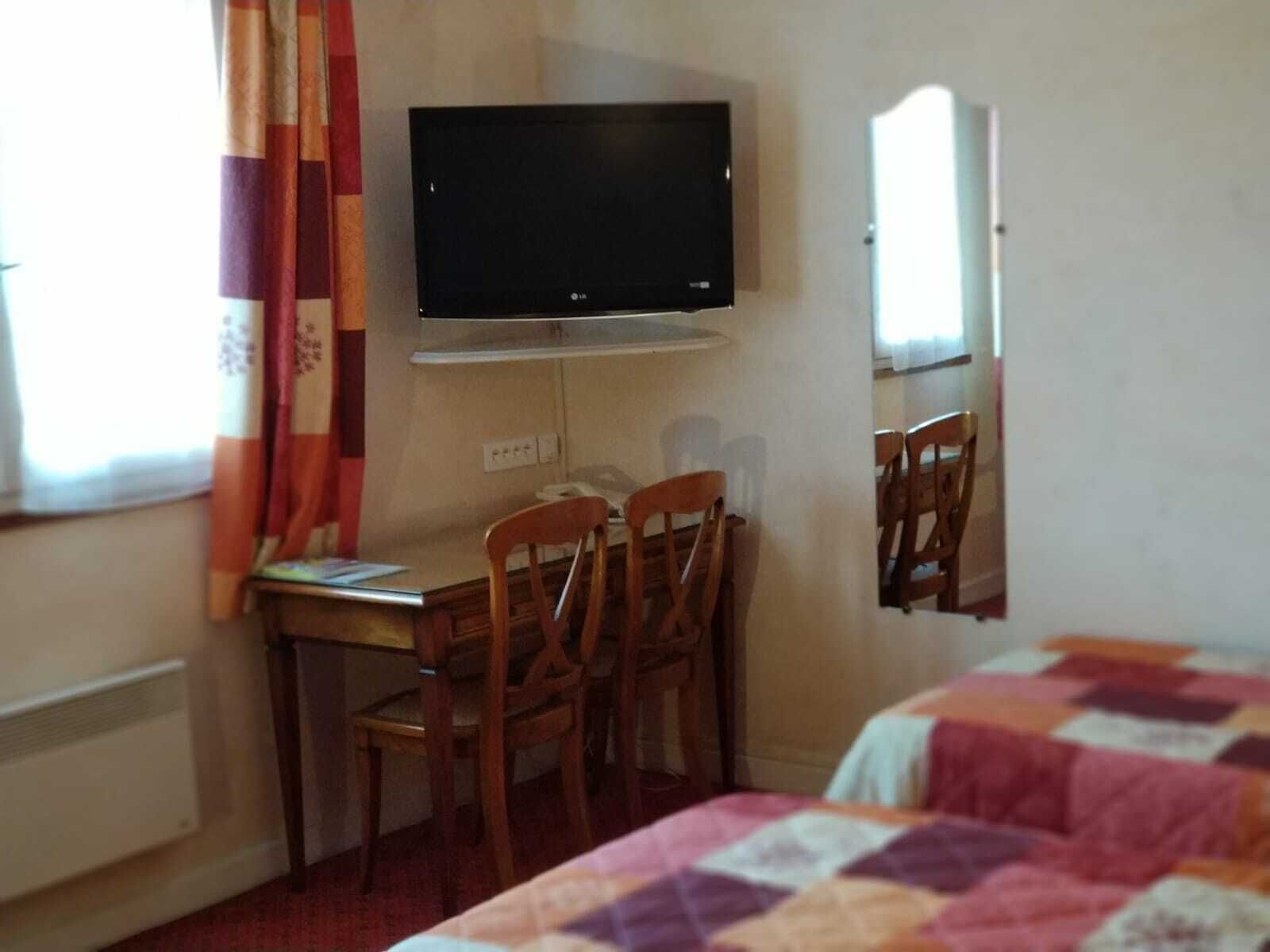 A hotel room with a bed, a desk with two chairs, a television, and a mirror.