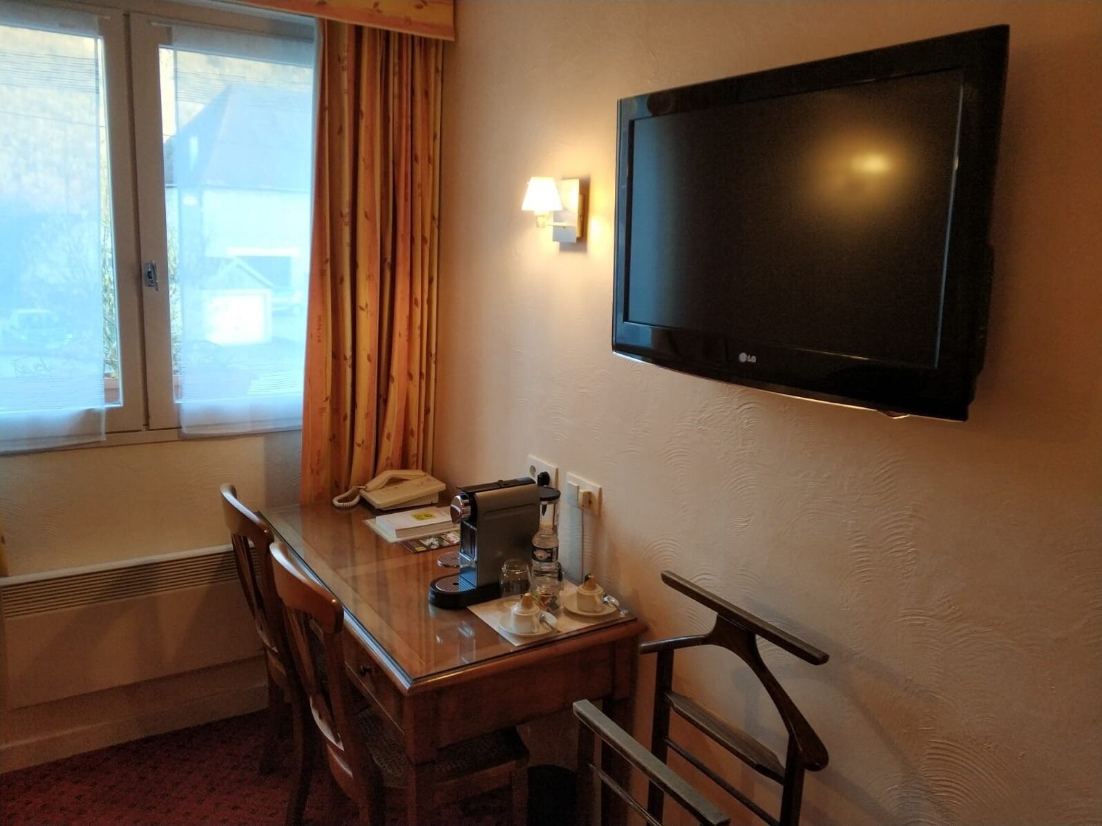 Habitación de hotel con un escritorio de madera, un teléfono, cafetera y televisor montado en la pared.