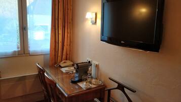 Habitación de hotel con un escritorio de madera, un teléfono, cafetera y televisor montado en la pared.