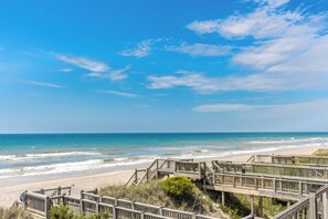 A beach with wooden boardwalks leading to the shore, clear skies, and calm ocean waves.