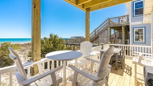 A wooden deck with white chairs and tables, overlooking a beach and ocean.