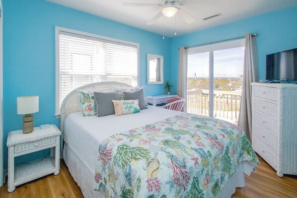 A bedroom with a bed, a nightstand, a dresser, a television, and a balcony with a view.