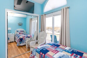 A bedroom with two beds, a TV, a chair, and a view of the outside. - Misty Morning South - Oceanfront 4BR Home; Dog Friendly! (Surf City)