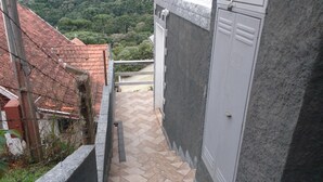A narrow pathway leading to a building with a tiled roof and a grey wall.