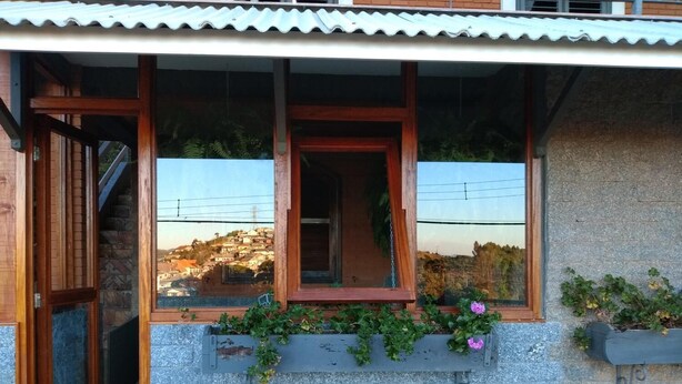 A stone building with a wooden door and windows, a stone staircase, and a view of a hillside.