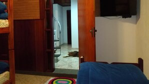 A room with a wooden door, a bed, a television mounted on the wall, and a visible staircase leading to another room.