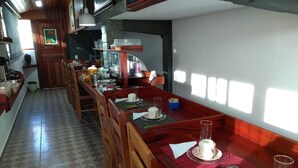 A long wooden dining table with chairs, a kitchen area with cabinets and appliances, and a tiled floor.