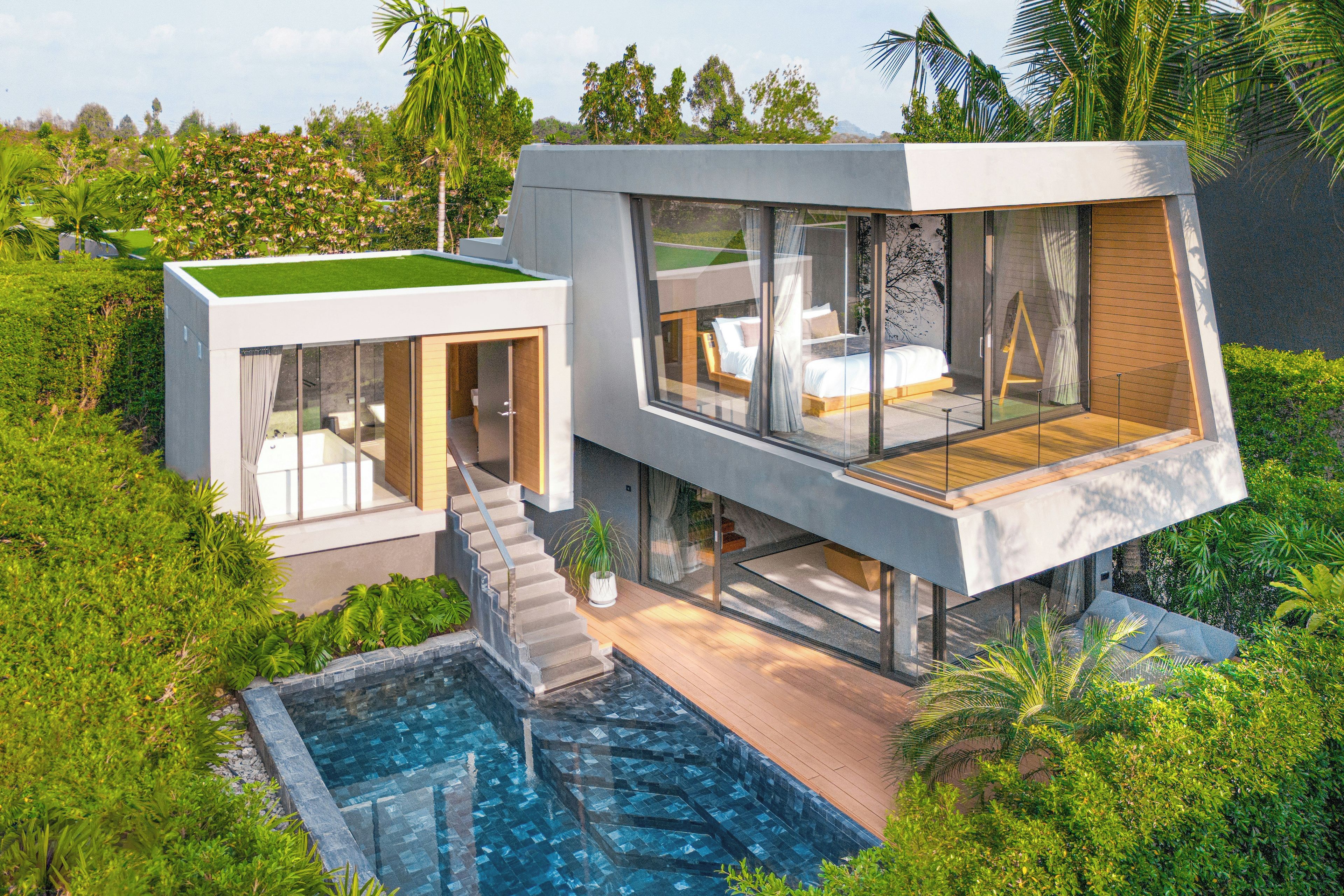A modern house with a glass facade, a swimming pool, and a lush garden.