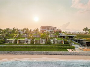 A beachfront resort with modern villas, a central building, and a sandy beach.