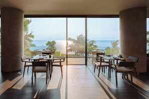 Un espace repas avec des tables et des chaises, de grandes fenêtres et une vue sur la mer.