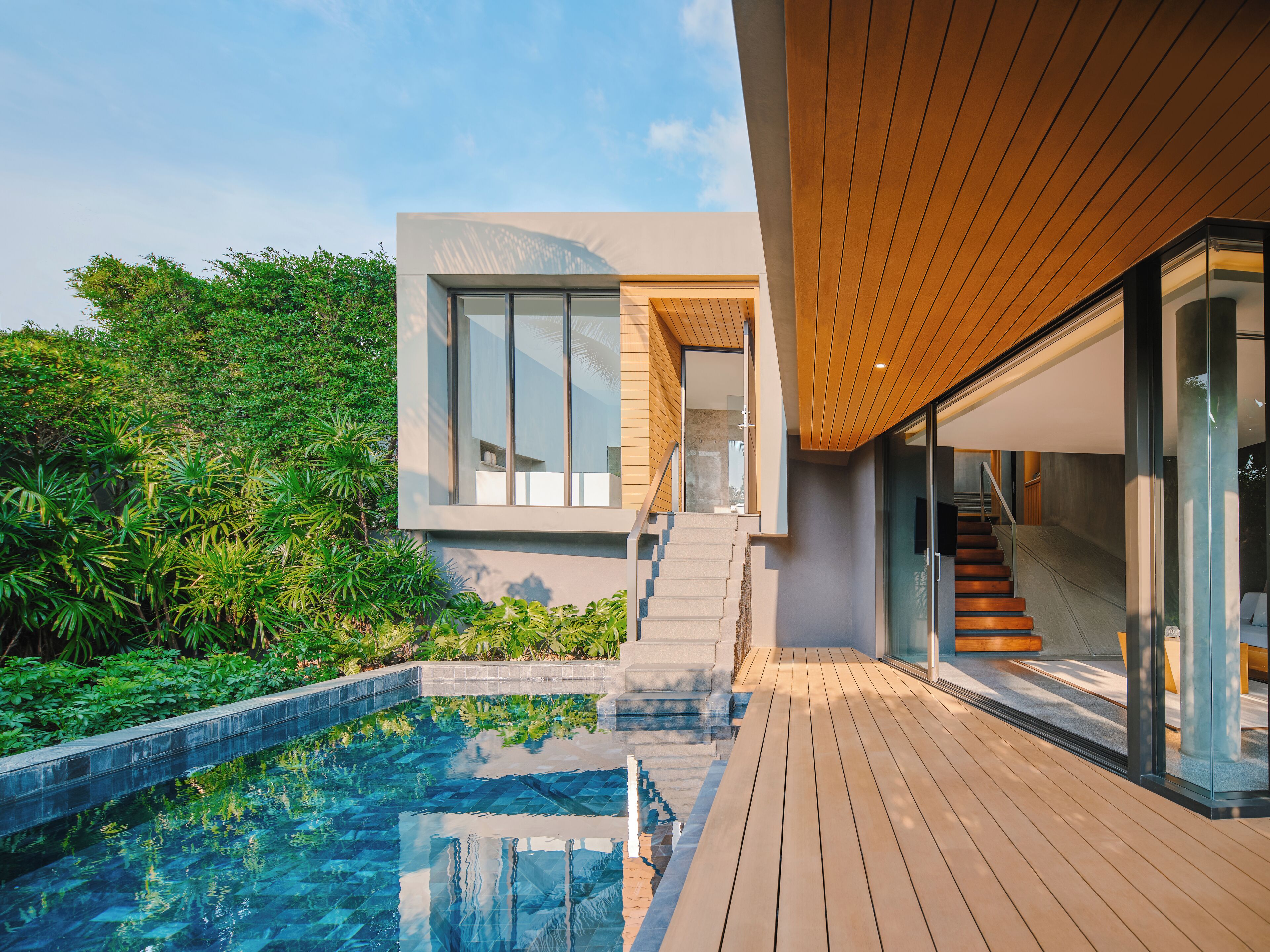 Una casa moderna con piscina, terraza de madera y una escalera que conduce a una puerta de cristal.