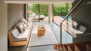 A modern living room with a sofa, coffee table, and a view of an outdoor deck and pool. - MASON, a member of Design Hotels (Sattahip)
