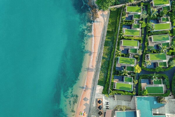 An aerial view of a coastal resort with a beach, multiple hotel buildings, and a clear view of the ocean.