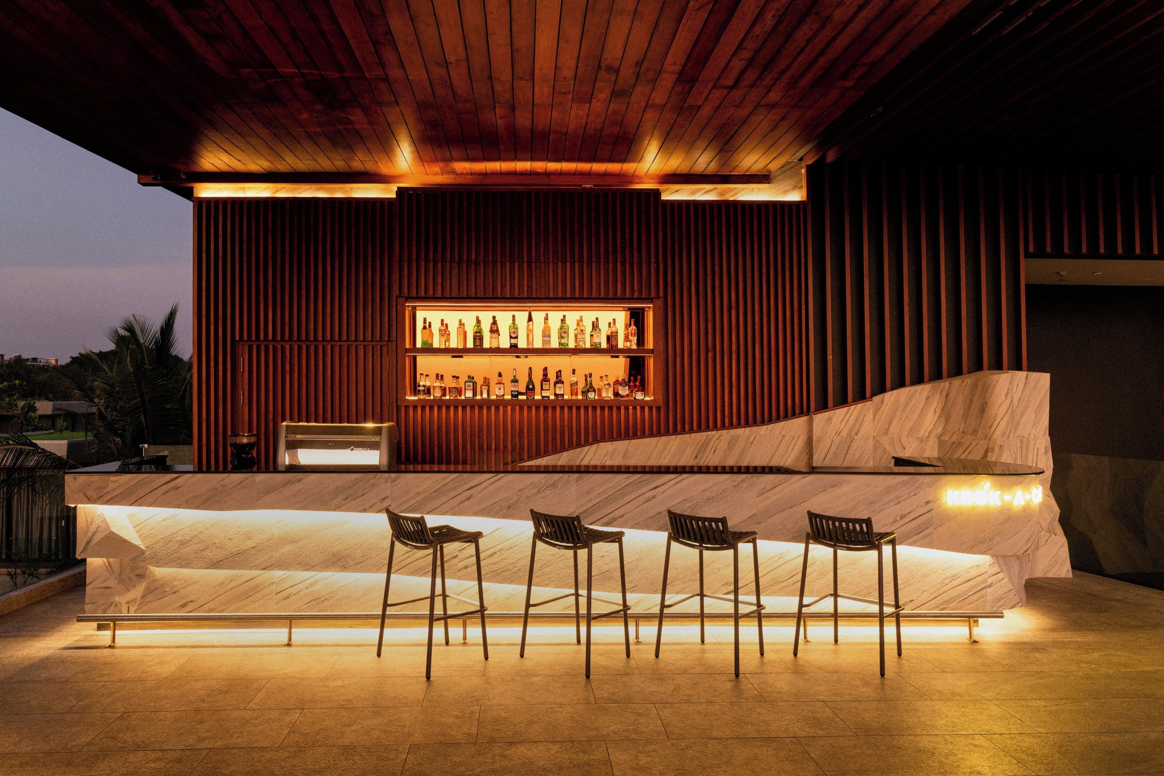 An outdoor bar area with a long counter, multiple chairs, and a wooden ceiling.