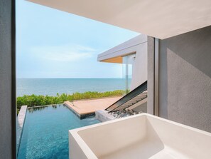 Piscina infinita moderna con vista al océano, una bañera blanca y una escalera que conduce a un balcón.