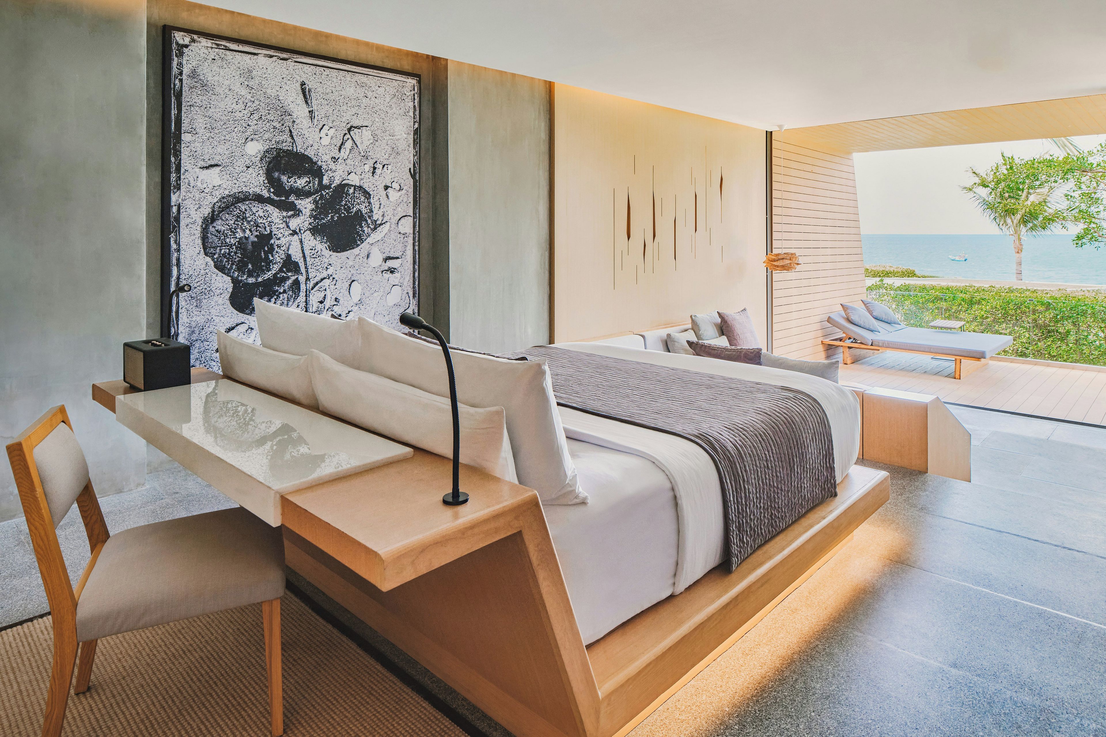 A modern bedroom with a large bed, a desk, and a view of the sea.