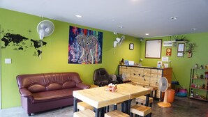 A room with a green wall, a wooden table with benches, a leather couch, and a world map decoration. - OYO 730 Meedee Hostel (Bangkok)