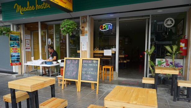 A hostel exterior with wooden tables and benches, a chalkboard menu, and a neon 'OPEN' sign. - OYO 730 Meedee Hostel (Bangkok)
