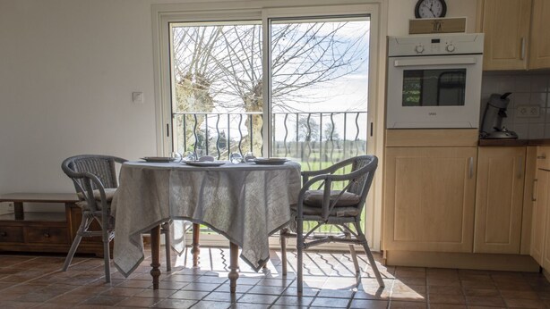Un comedor con una mesa lista para cuatro, una cocina con armarios de madera y un amplio ventanal con vista a árboles.